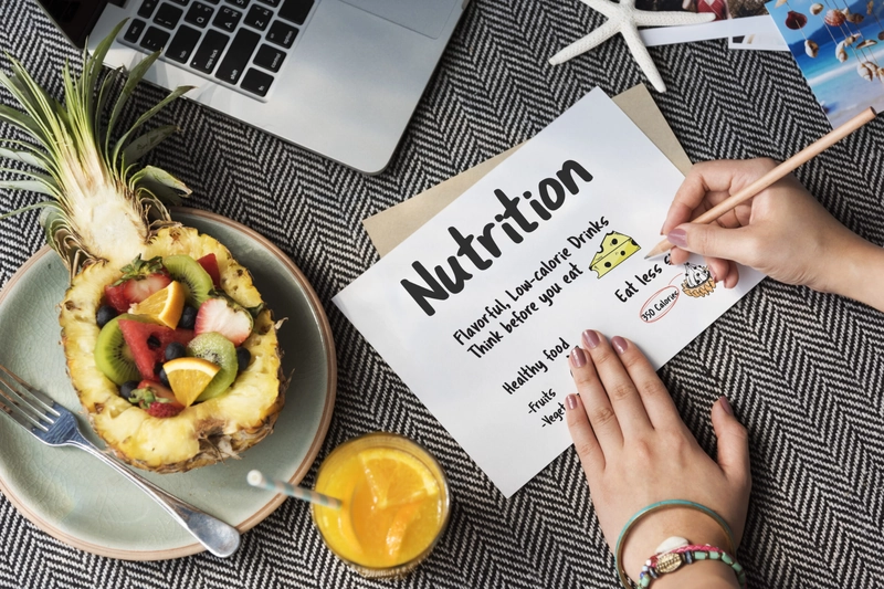 Tờ ghi chú đề chữ Nutrition bên đĩa trái cây trong vỏ dứa và ly nước cam, minh họa nutrition ingredients