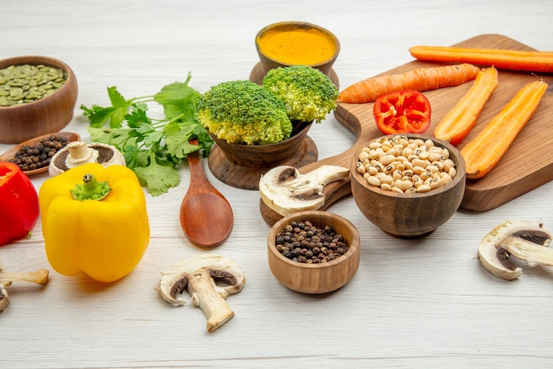 Ớt chuông vàng, bông cải xanh, cà rốt, nấm và chén bột nghệ bày quanh thớt gỗ trên nền trắng