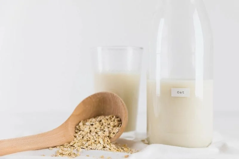 Ly sữa yến mạch và chai ghi chữ Oat đặt cạnh thìa gỗ đựng yến mạch cán, nhóm nutrition ingredients thực vật