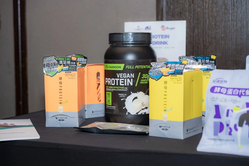 Hũ bột đạm thuần chay và các hộp sản phẩm Yeast Protein bày trên bàn trưng bày tối màu